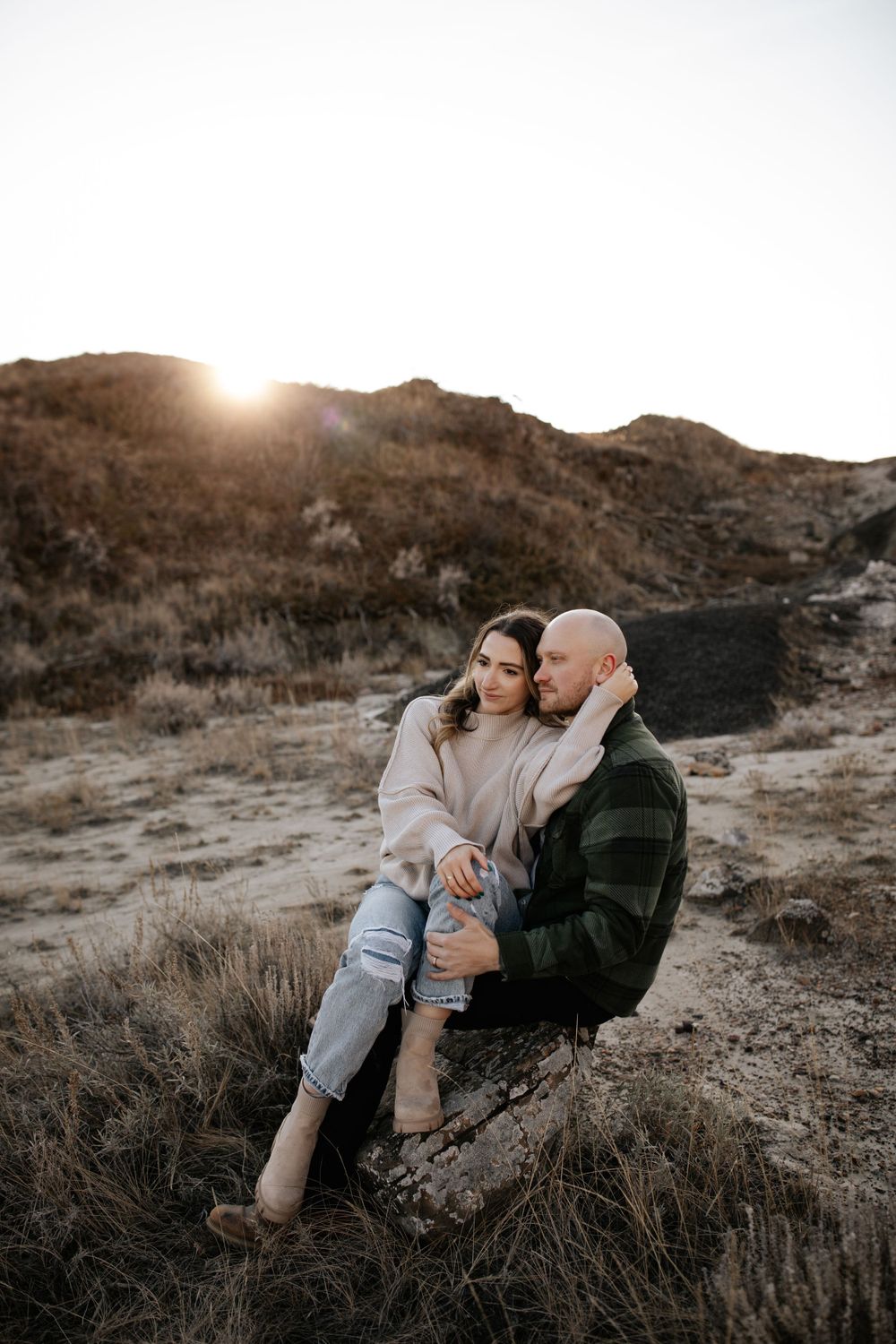A couple sits together on a rocky hill during golden hour.