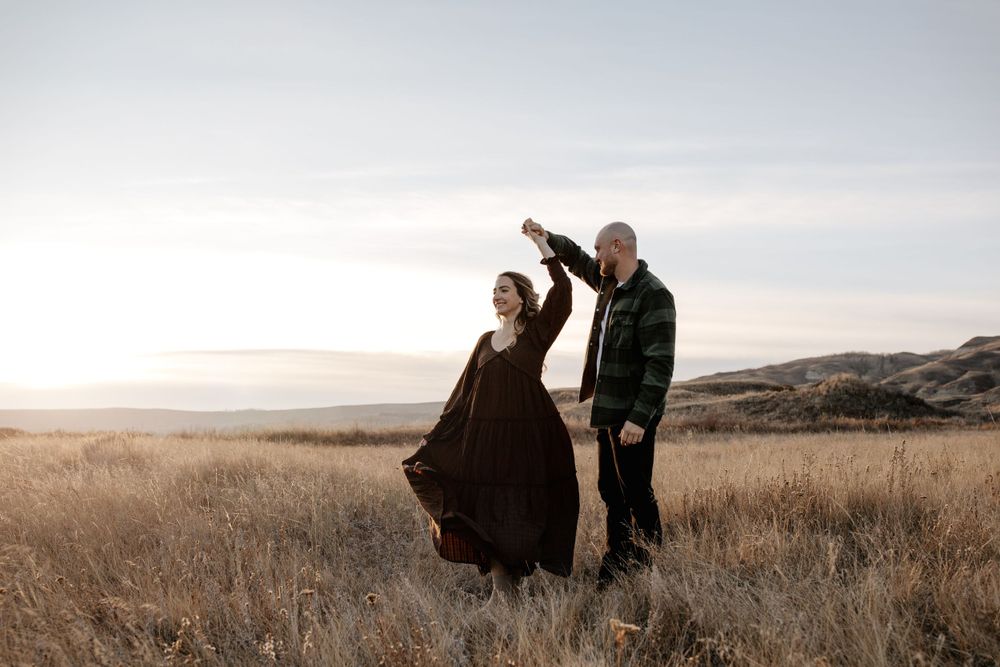 A couple poses together in a scenic grassland landscape at sunset.