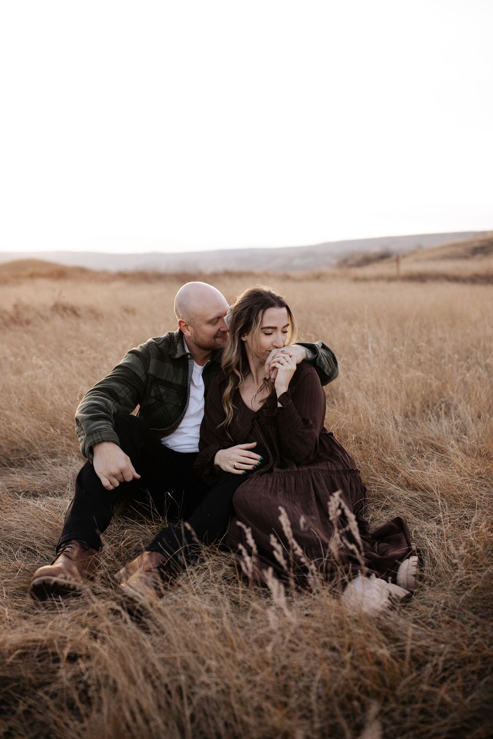 A couple relaxes together in tall grass during a golden sunset.