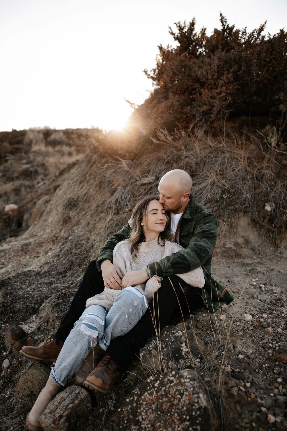 A couple relaxes together on a rocky hillside during sunset.