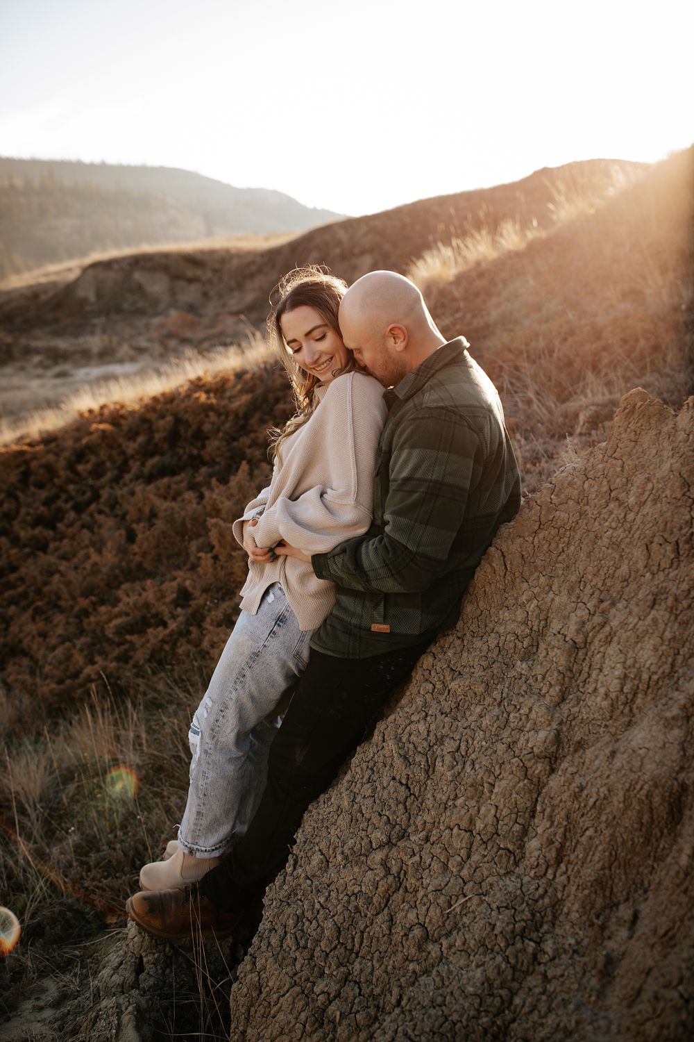 Two people cuddle intimately against a rocky cliff during golden hour.