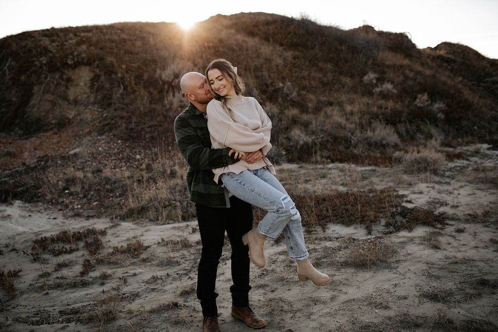 A couple shares playful moments on rocky terrain at sunset.