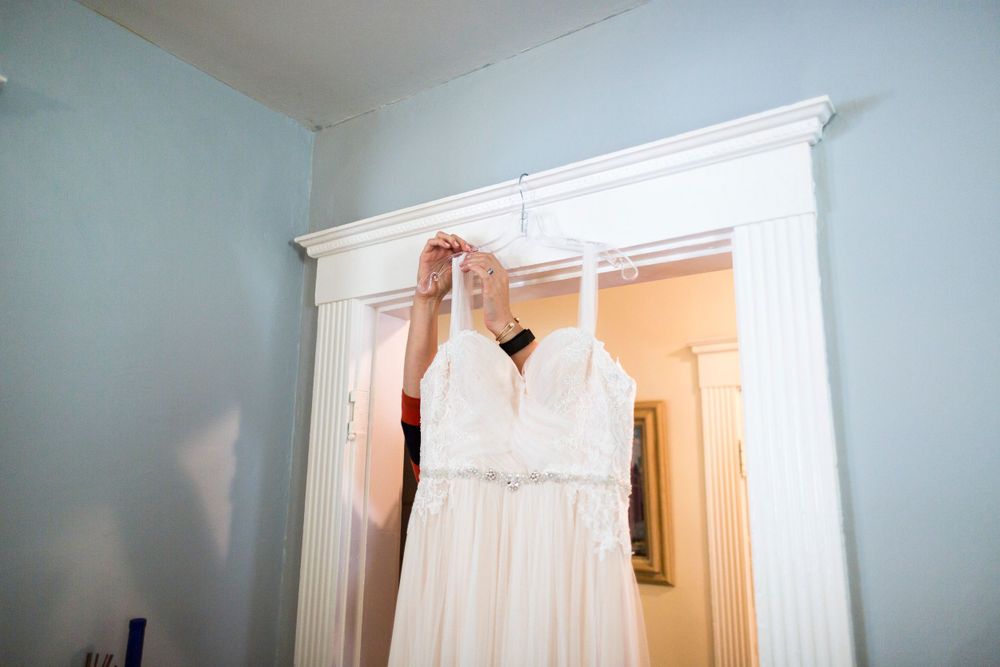 White lace wedding dress hanging on a doorframe in a light blue room.