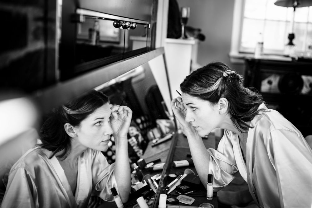 Black and white photo of bridesmaids applying makeup at a vanity mirror.