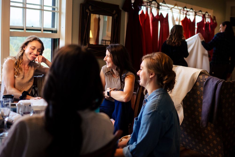 Bridesmaids laugh and chat during hair and makeup preparations before wedding ceremony.
