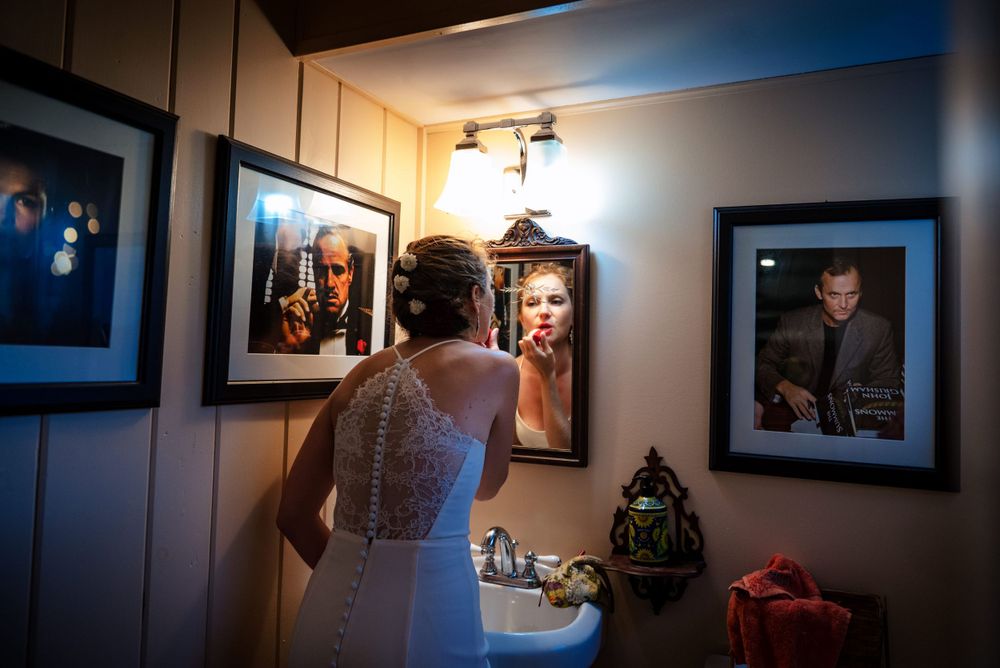 Bride in lace wedding gown applying lipstick in a mirror before her wedding.