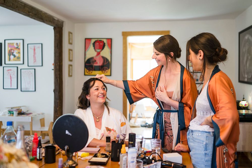 Bridesmaids laughing and chatting during bridal preparations at a makeup vanity table with cosmetics.