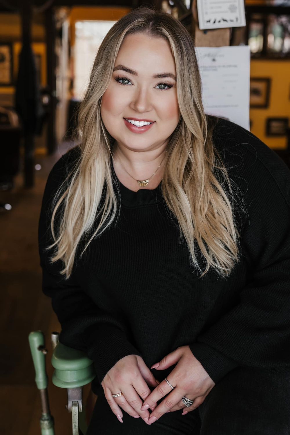 Portrait of someone in black sweater with long blonde hair sitting in casual indoor setting.