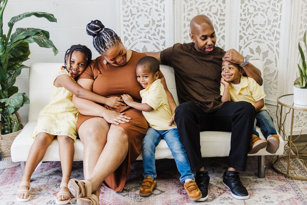 A loving family snuggling together on a couch with matching yellow outfits and a decorative plant in the background.