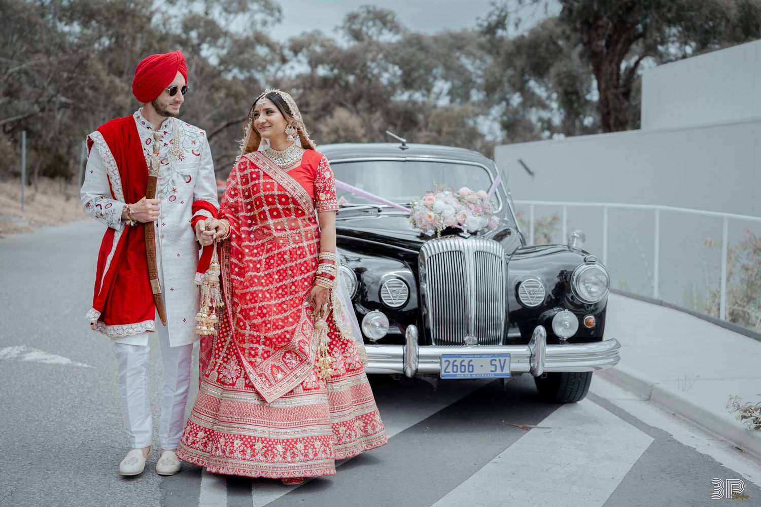 Bride and groom posing next to a vintage car, adding a retro touch to their wedding portrait with classic elegance.