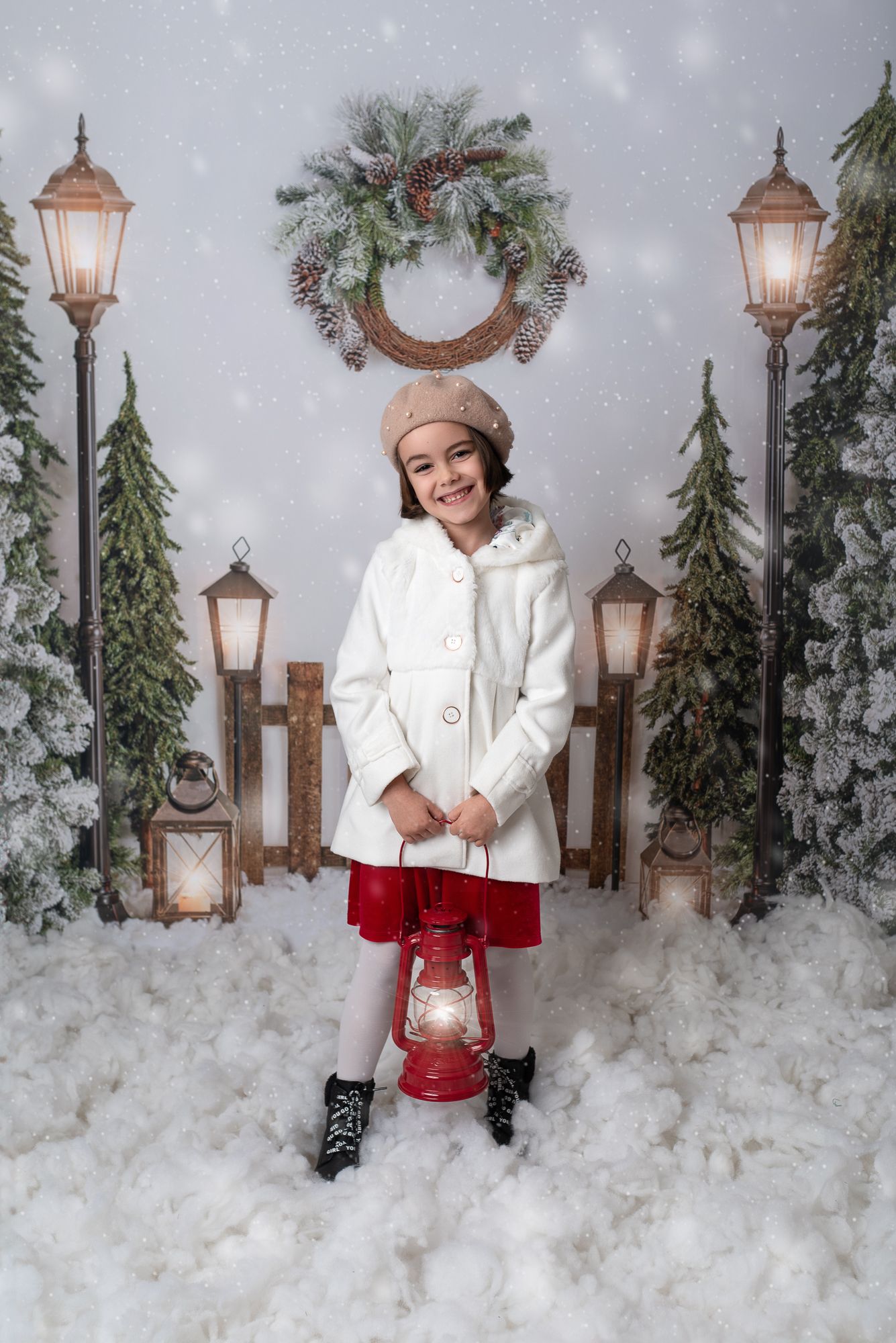 A winter scene with a glowing lantern surrounded by snow, evergreen trees, and holiday decorations in a studio setting.