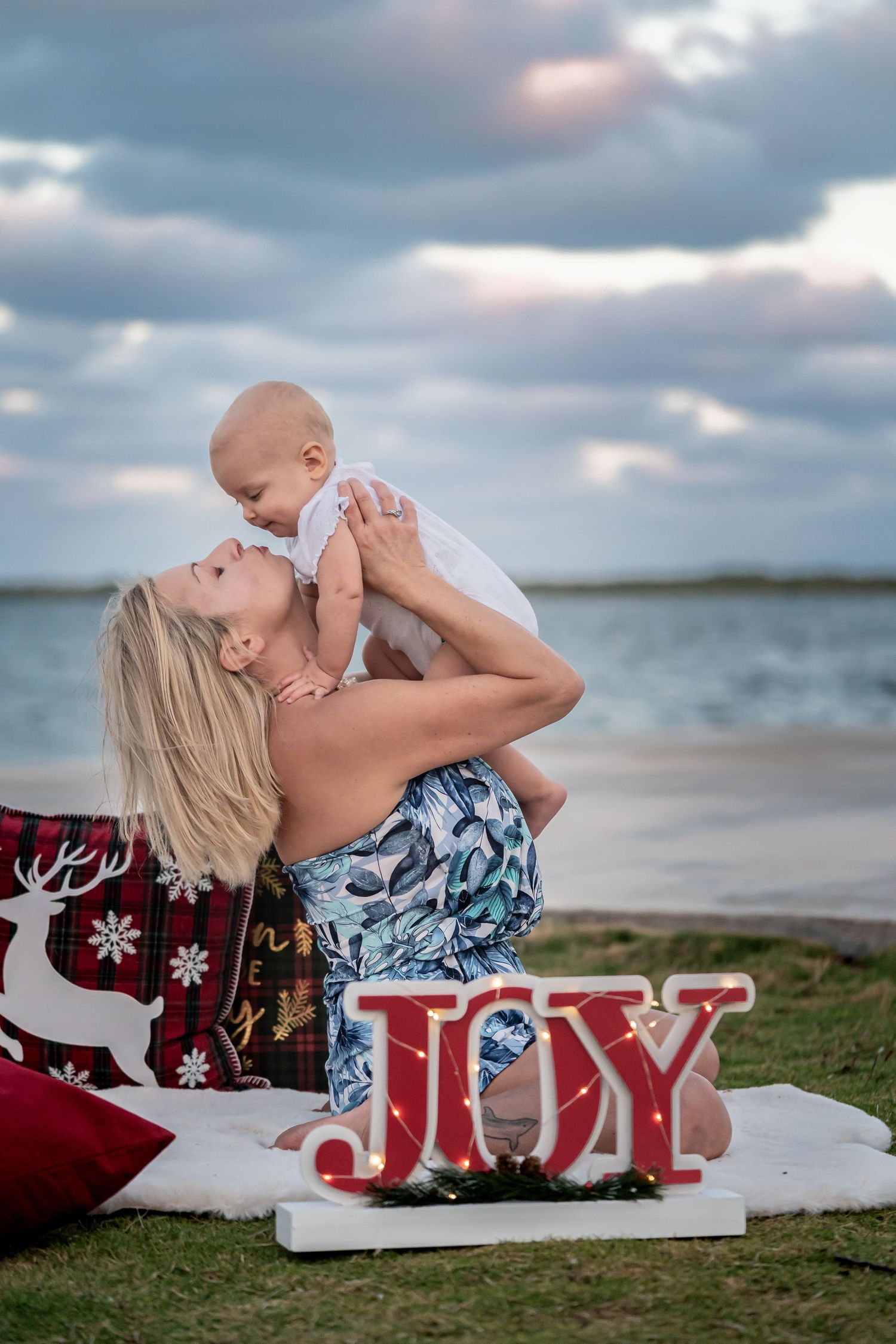 A beach photoshoot series with a red and white 'LOVE' sign decorated for Christmas with someone on a blanket.