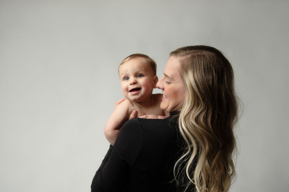 Mother and baby share joyful moment against light gray studio backdrop.