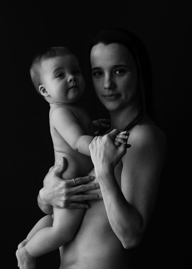 Intimate black and white portrait of parent and baby against dark background.