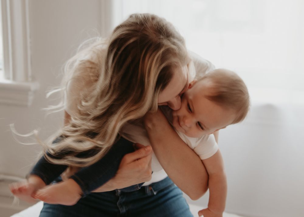 Candid moment between mother and baby by window in natural light.