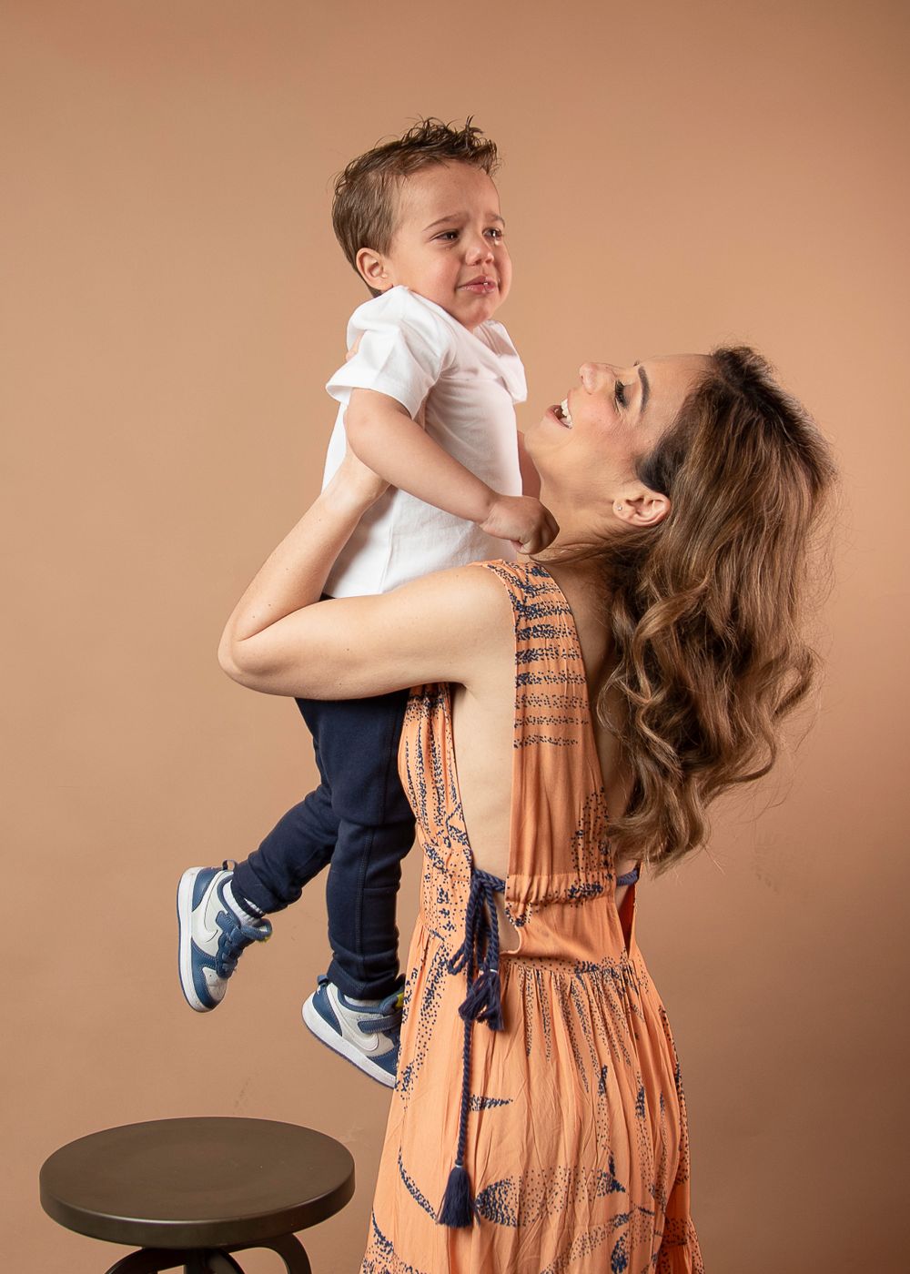 Playful studio portrait of mother lifting child in orange patterned dress.