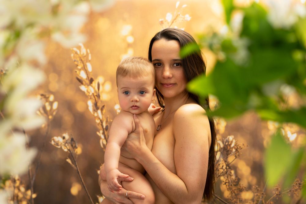 Ethereal outdoor portrait of parent and baby surrounded by golden sunlit foliage.