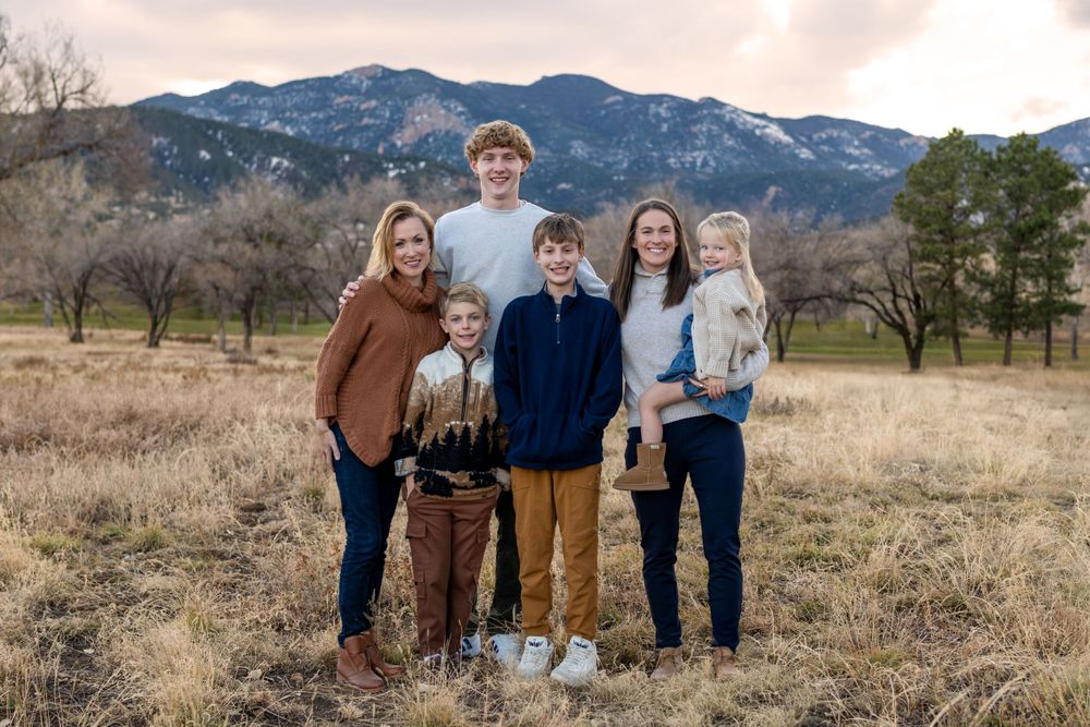 Family portrait in casual attire against mountain landscape at sunset.
