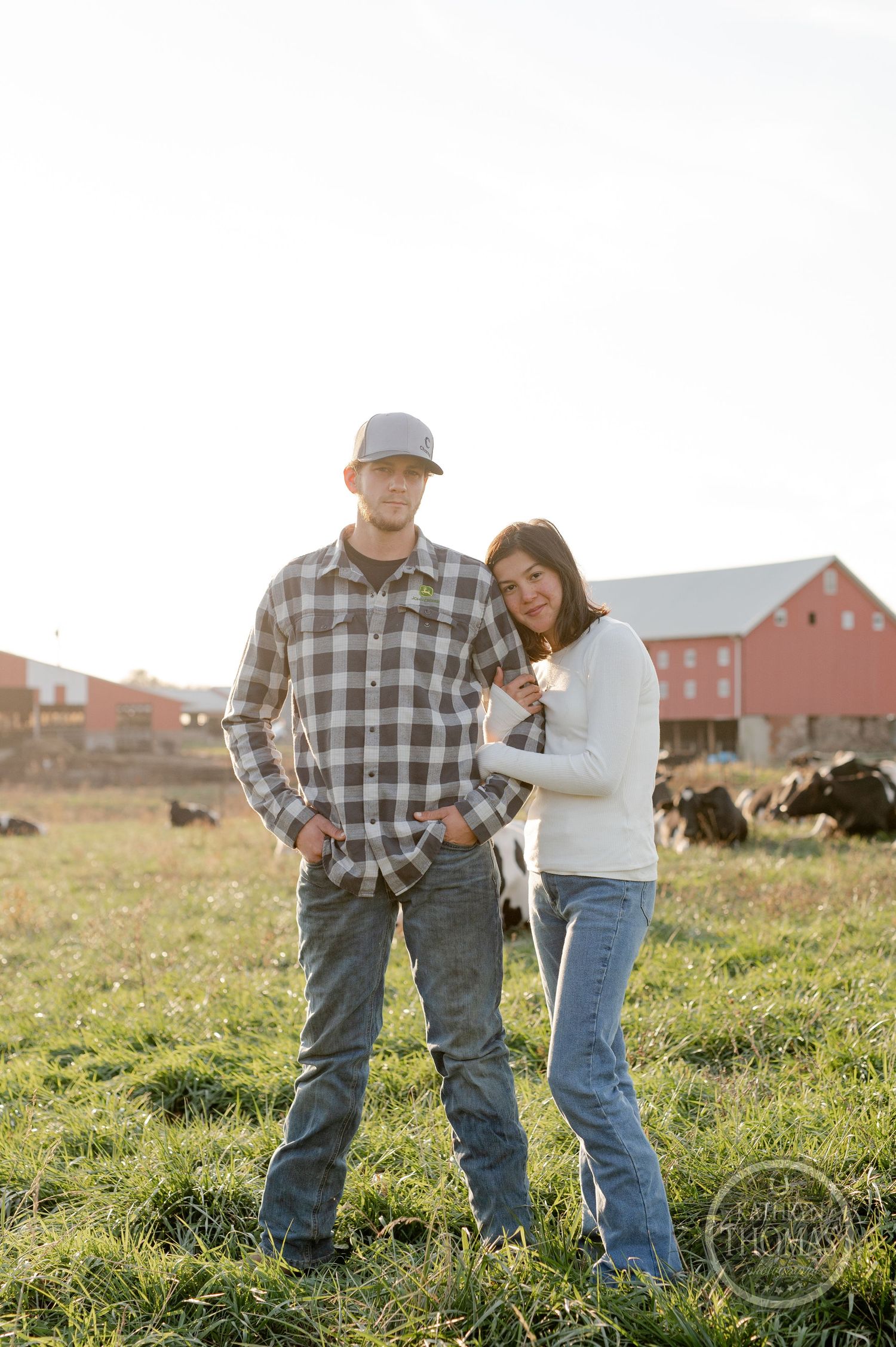 A casual farm photoshoot with a couple standing in a field near a red barn.