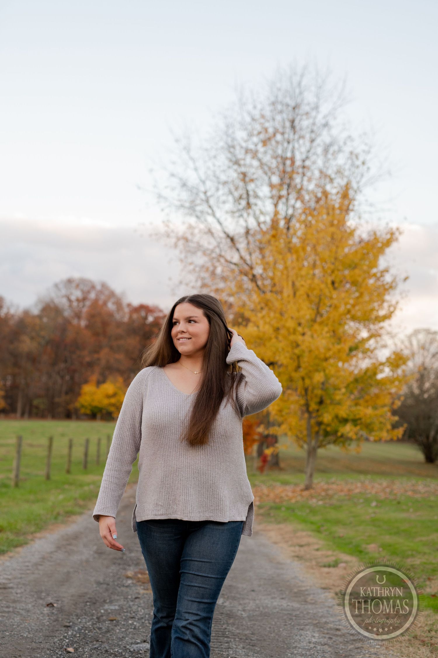 A casual outdoor portrait with golden autumn trees and green pastures in the background.