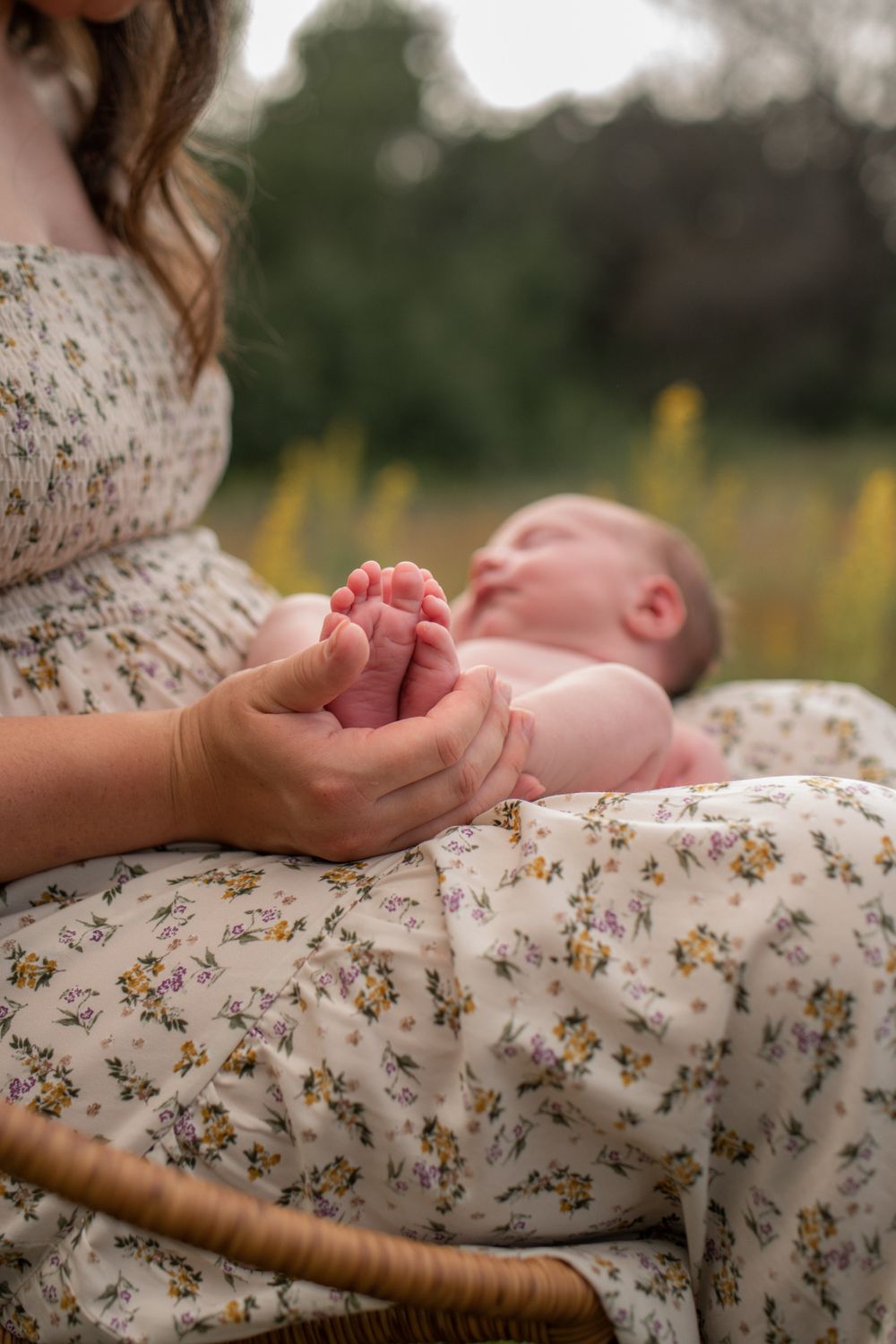 Close-up of tiny infant feet being held gently against a mother's floral dress.