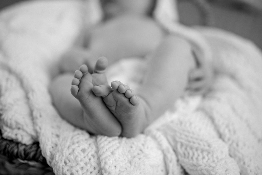 Close-up black and white photo of a newborn baby's tiny feet resting on soft lace fabric.