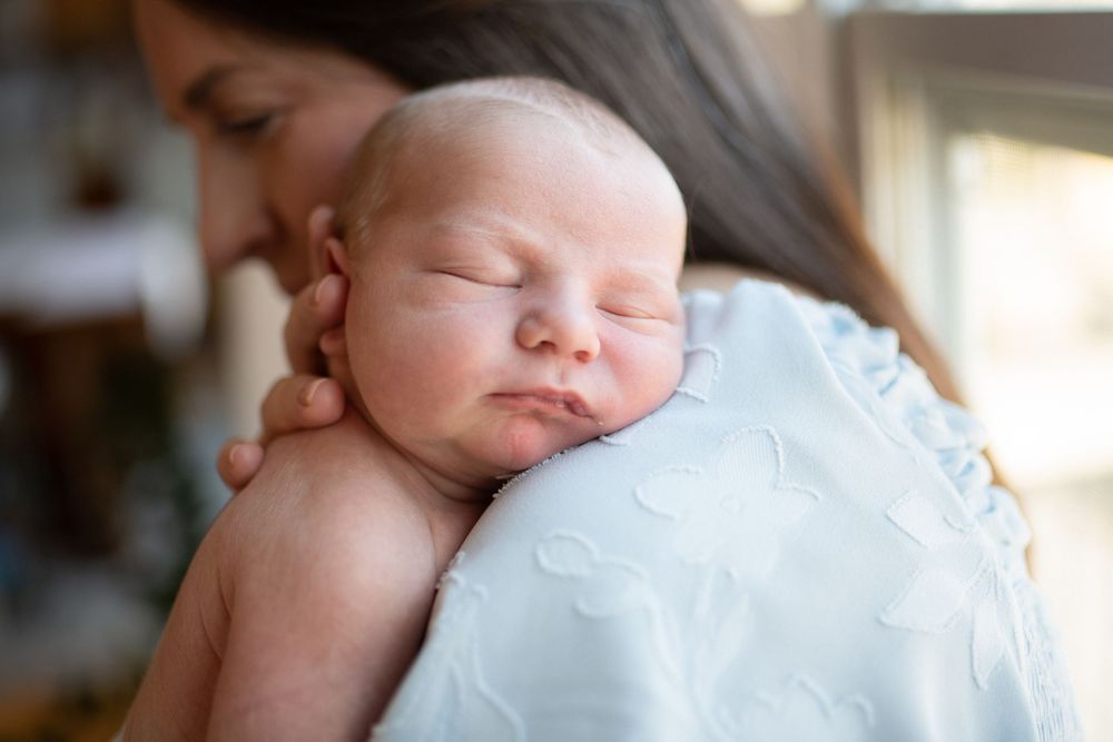 A peaceful sleeping baby wrapped in soft white blankets rests in natural window light.