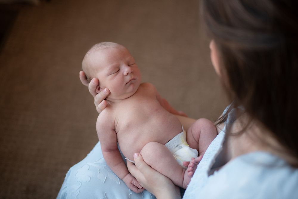 A newborn baby receives gentle care while lying on a soft white blanket during a tender moment.