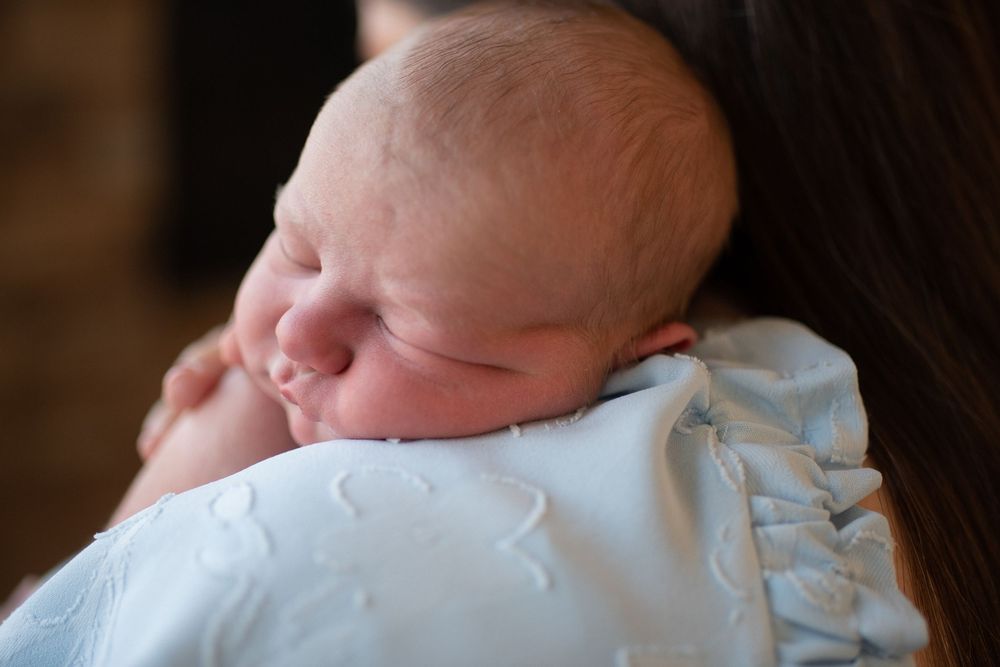 A newborn baby's tiny feet wearing white socks are gently held by adult hands against a dark background.