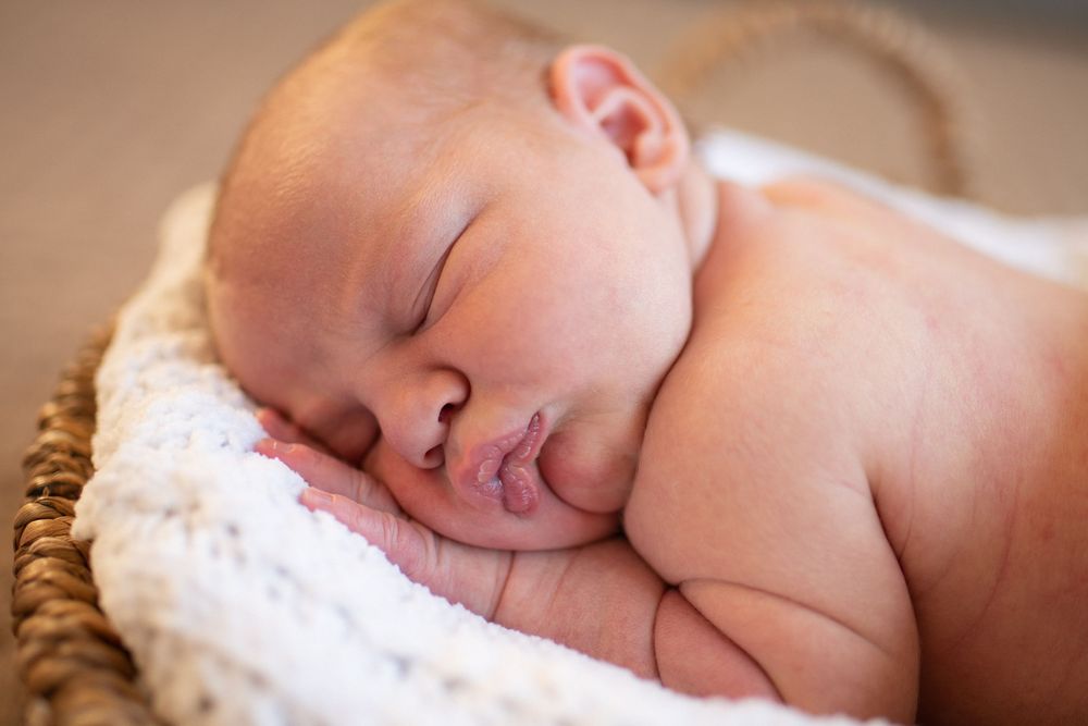 Peaceful sleeping newborn baby wrapped in soft white blanket resting on cozy brown fabric.