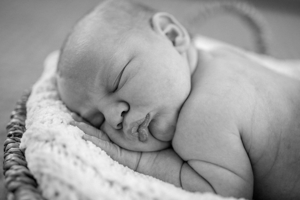 Peaceful black and white portrait of a sleeping newborn baby swaddled in soft fabric.