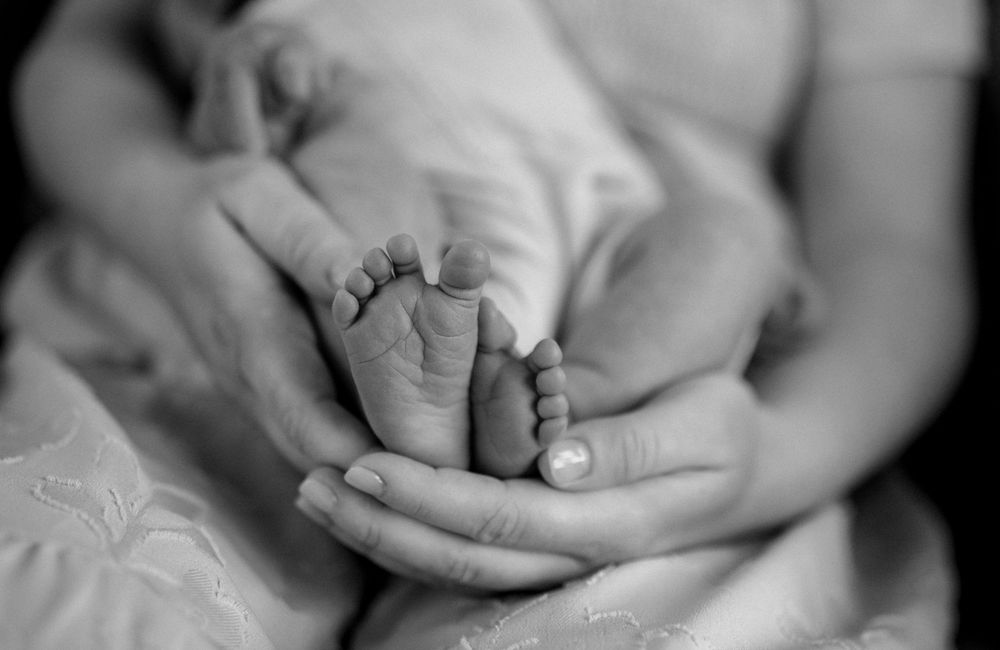 Black and white close-up photo showing hands tenderly holding a newborn baby's tiny feet.