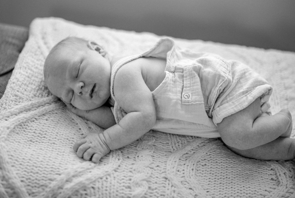Sleeping baby in black and white wearing overalls lies peacefully on a textured knit blanket.