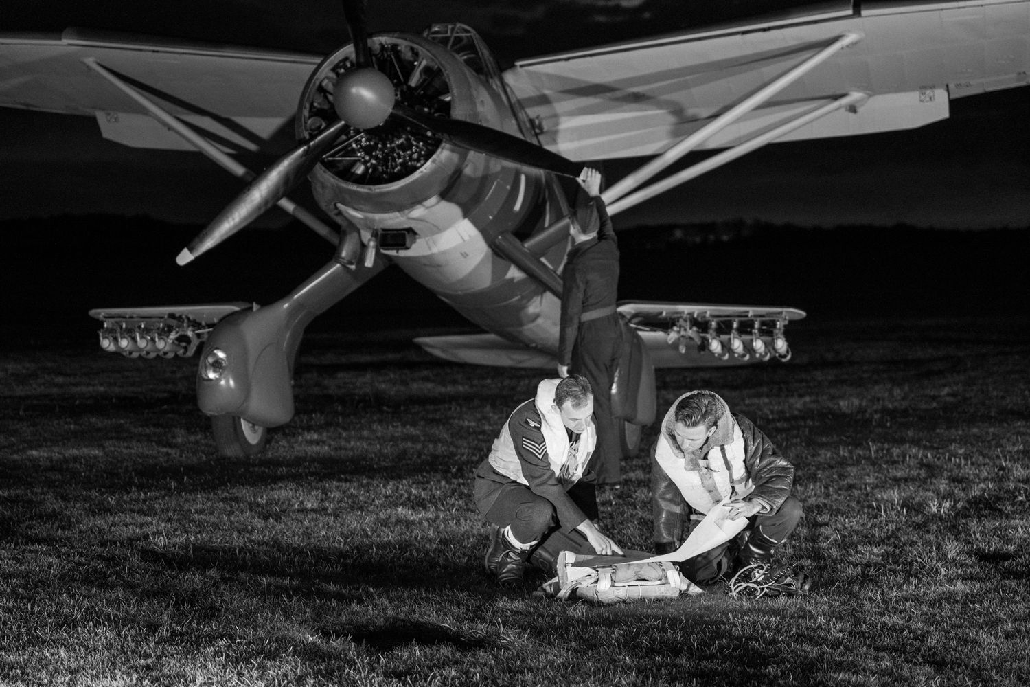 Black and white image of vintage aircraft with figures examining equipment on field.
