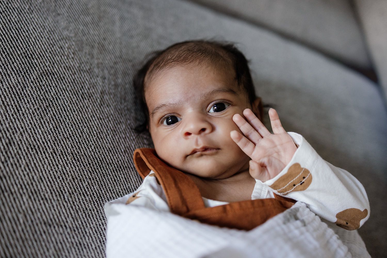 Alert baby waves at camera during in-home lifestyle newborn session in San Jose