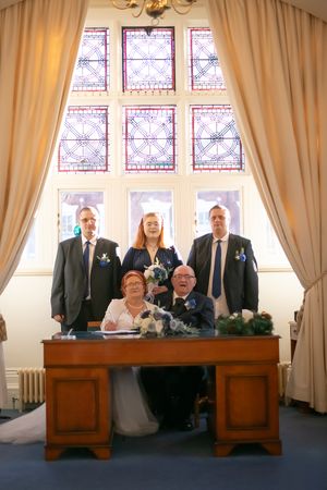 Wedding party poses in front of ornate stained glass windows behind an antique wooden desk.