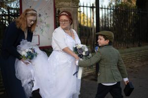 Wedding party in formal attire gathered outside with flowers and decorative gates.