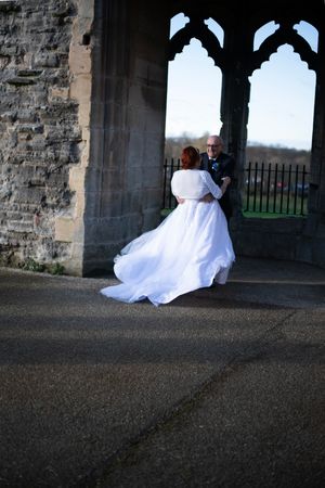 Bride's white dress twirls dramatically under historic stone archway.