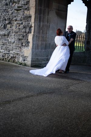 Wedding couple stands intimately together under gothic stone architecture.