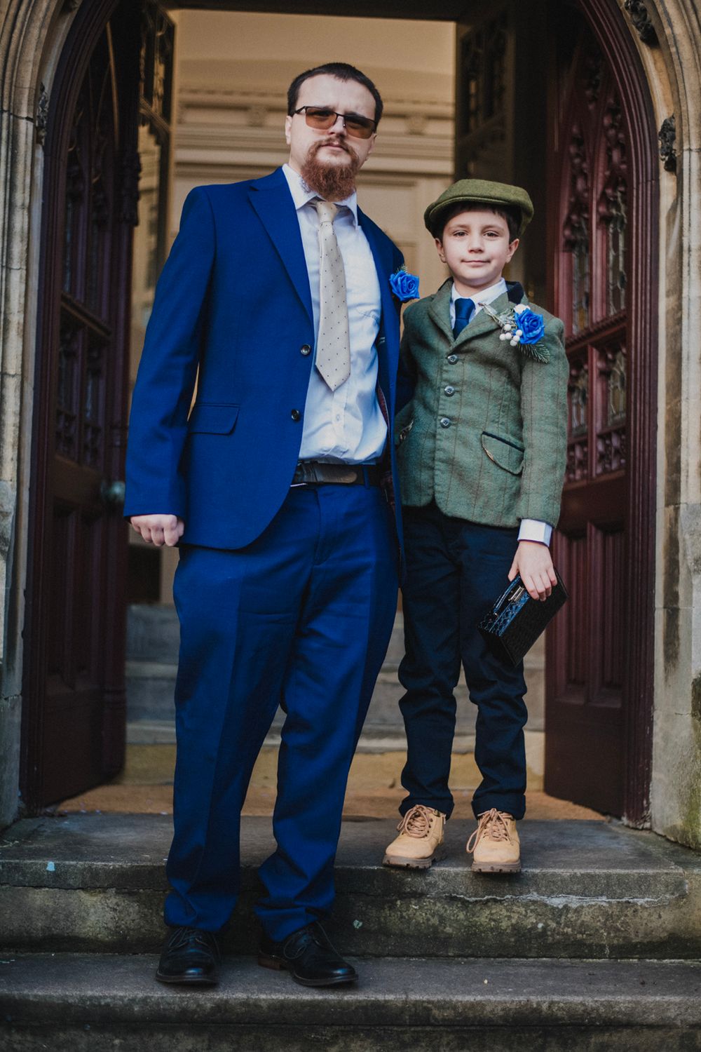Formal portrait of wedding attendees in blue suit and green tweed standing in gothic archway.
