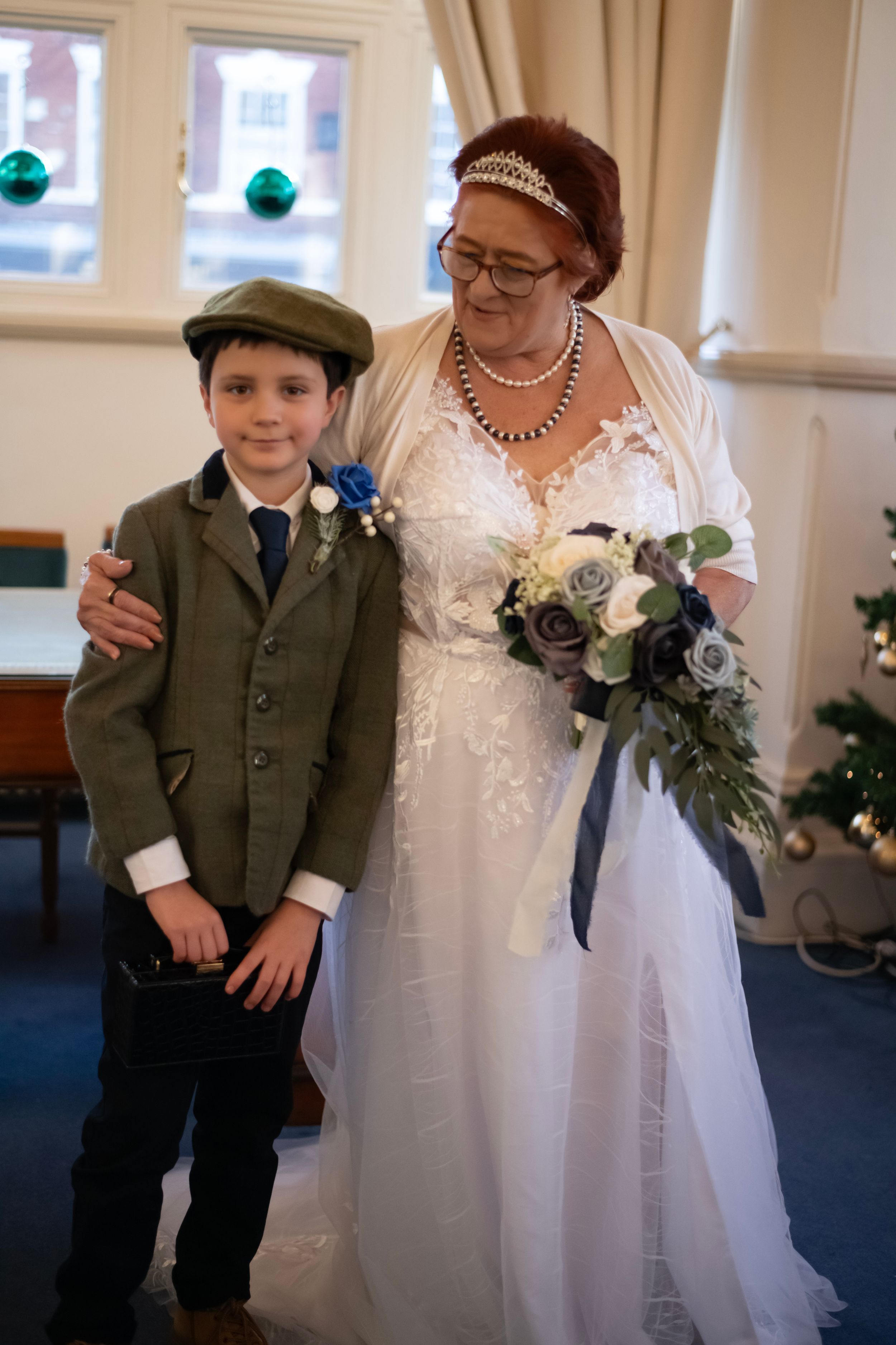 Wedding portrait featuring white dress and sage green suit against festive holiday backdrop.