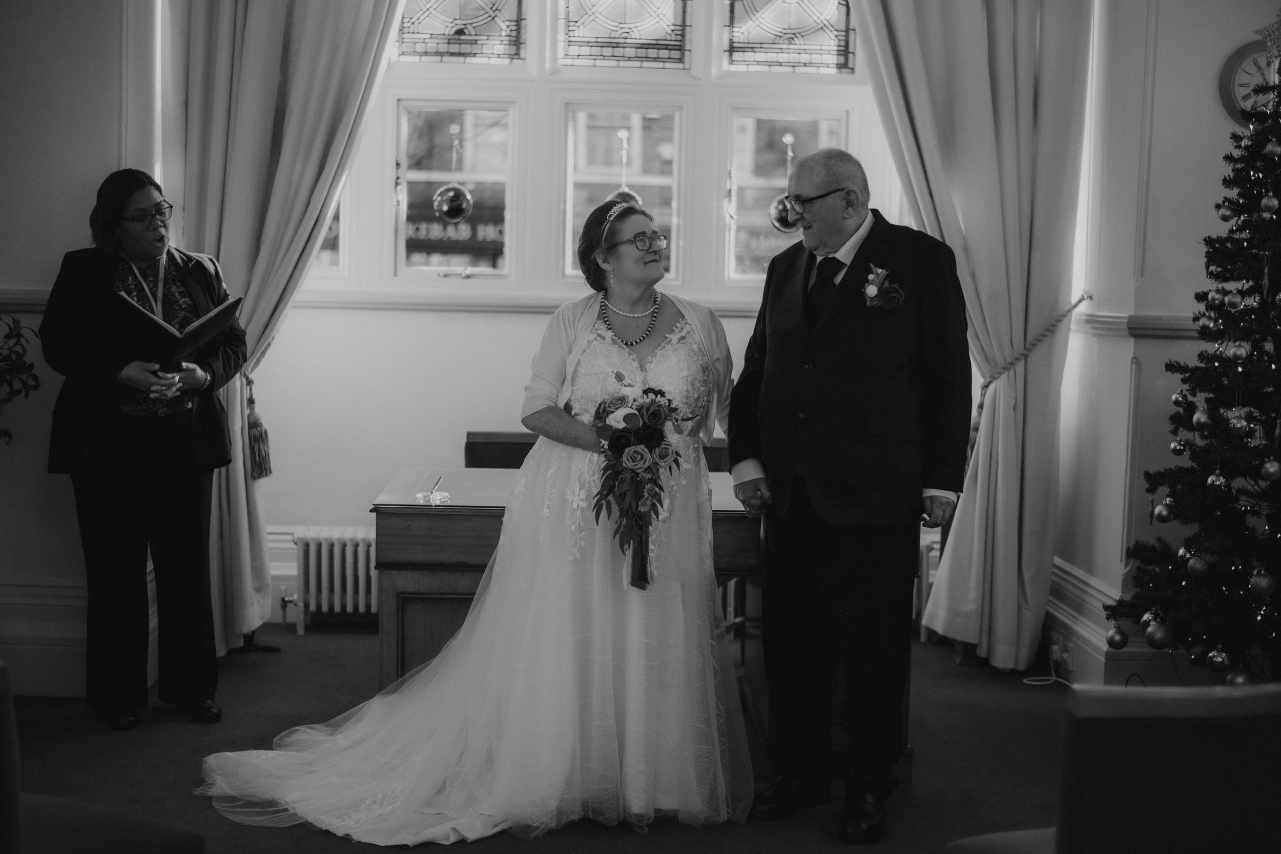 Black and white wedding photo showing a couple at the altar with their wedding party in an elegant indoor setting.