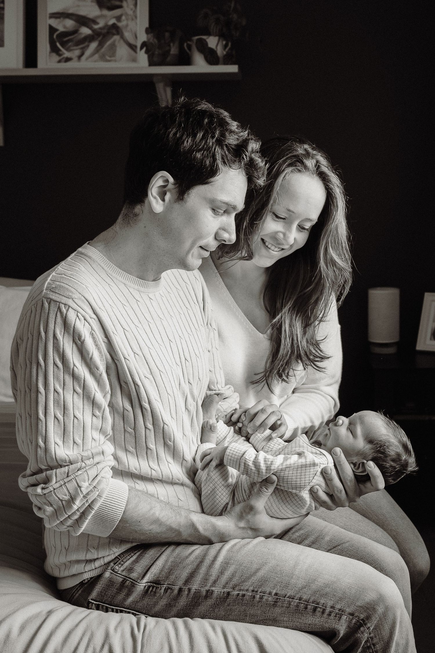 A tender family moment with parents cradling their newborn baby while wearing cozy sweaters in black and white.