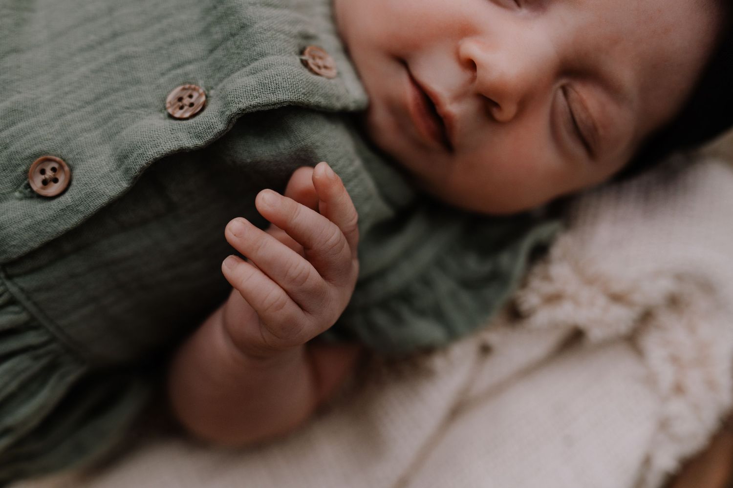 Close-up of a sleeping baby's tiny hand in soft, natural lighting.