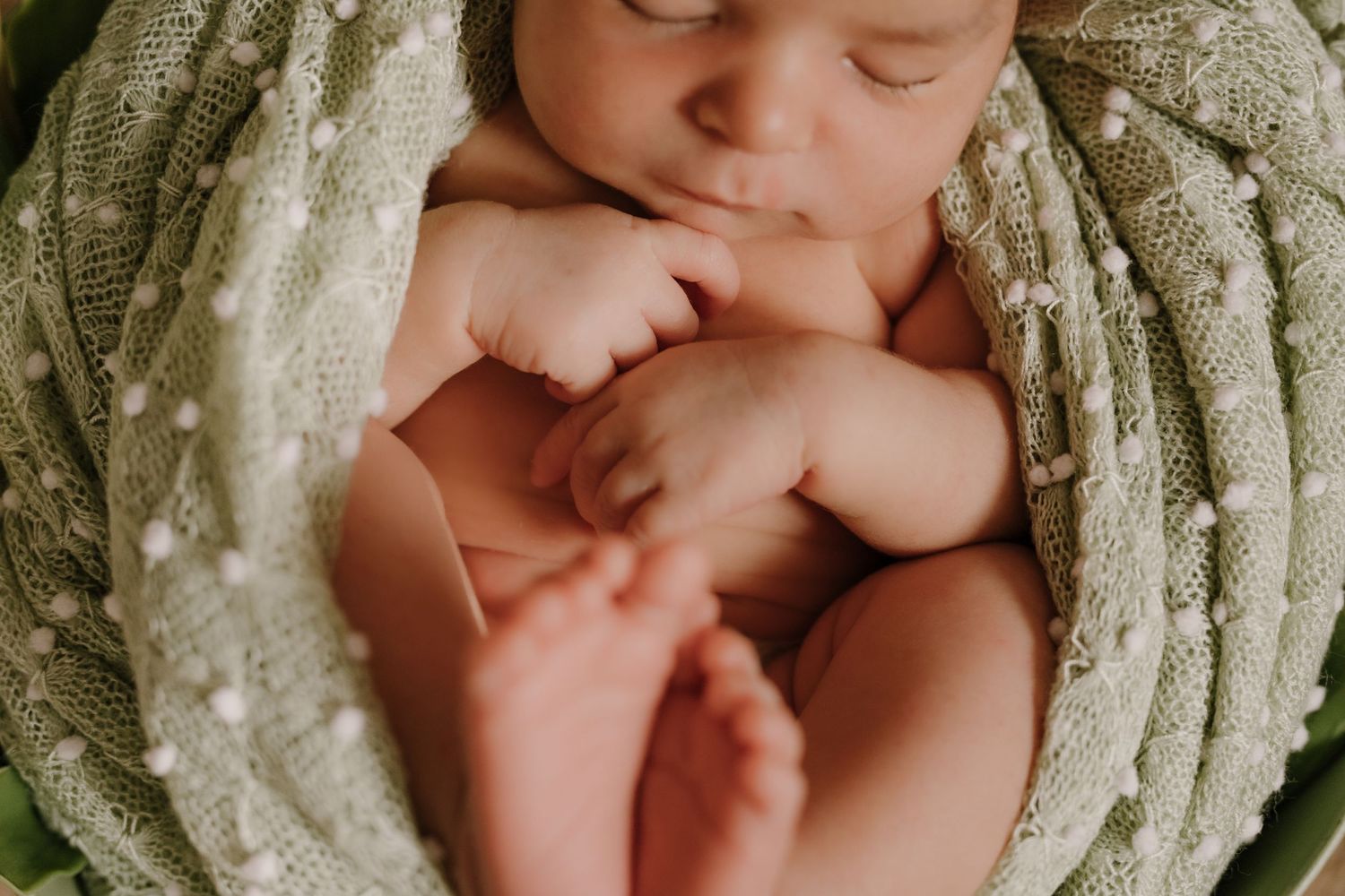Close up of a sleeping newborn curled up in a textured white wrap.