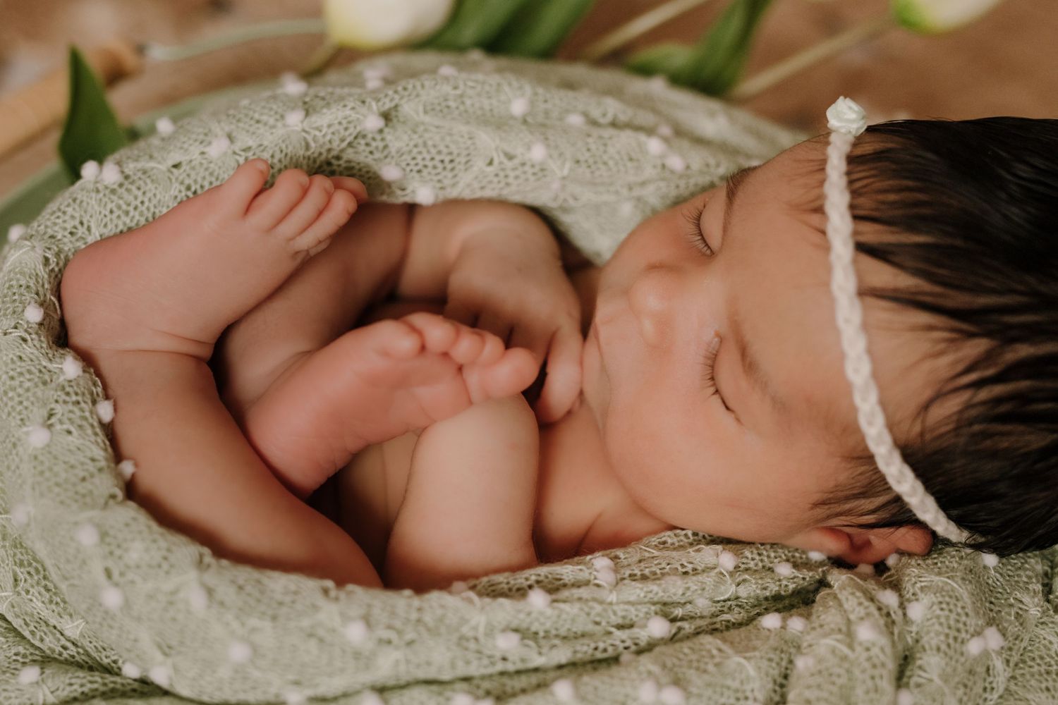 Sleeping newborn wrapped in delicate lace fabric with white headband.