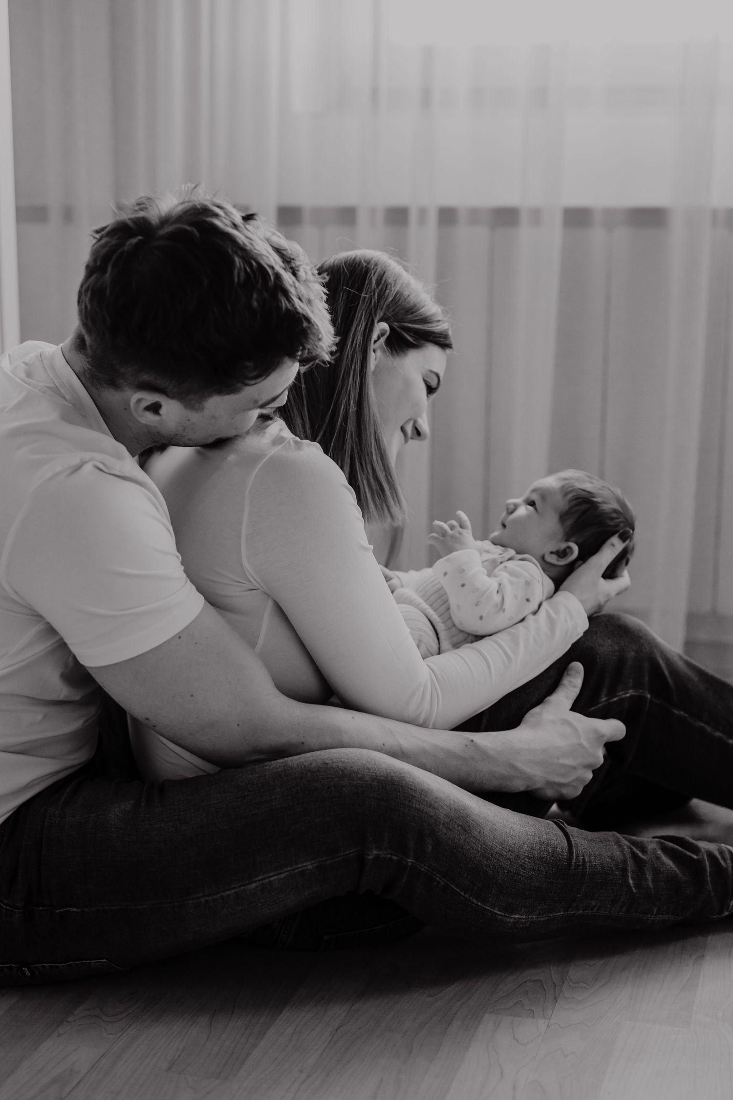 A black and white image of parents sharing an intimate moment with their newborn on the floor.
