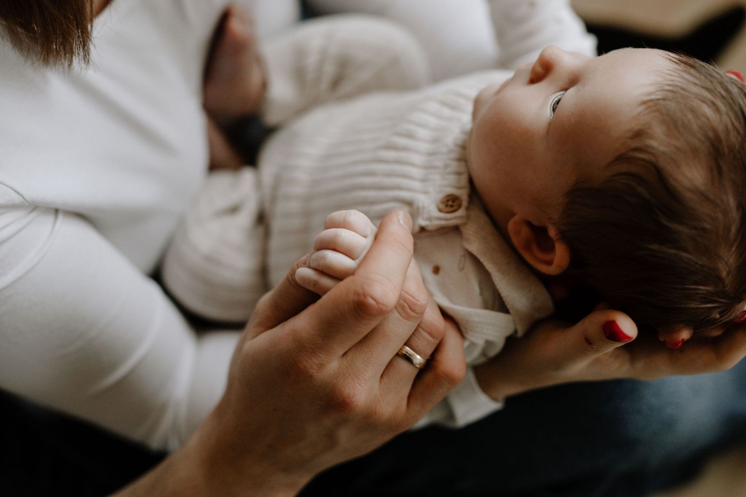 Close-up of hands holding sleeping baby dressed in neutral colors against white background.