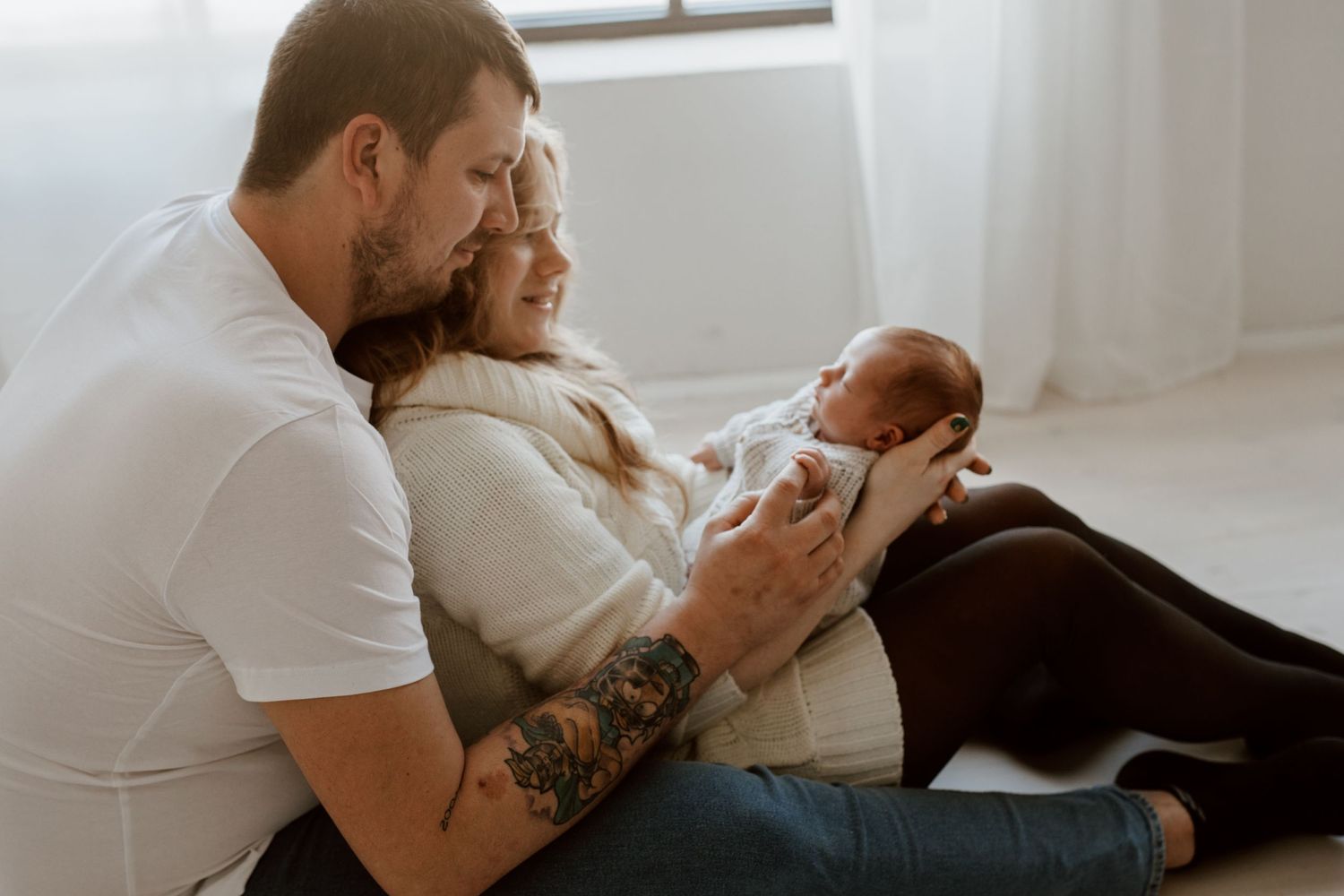 A couple snuggling with their newborn baby in a bright, sunlit room.
