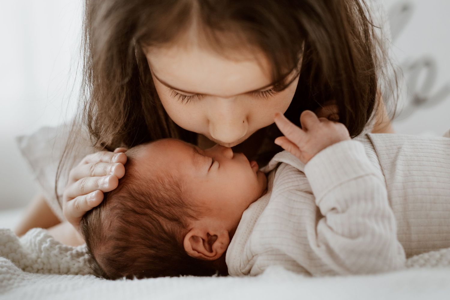 Intimate lifestyle portrait of siblings sharing a tender moment on white bedding.
